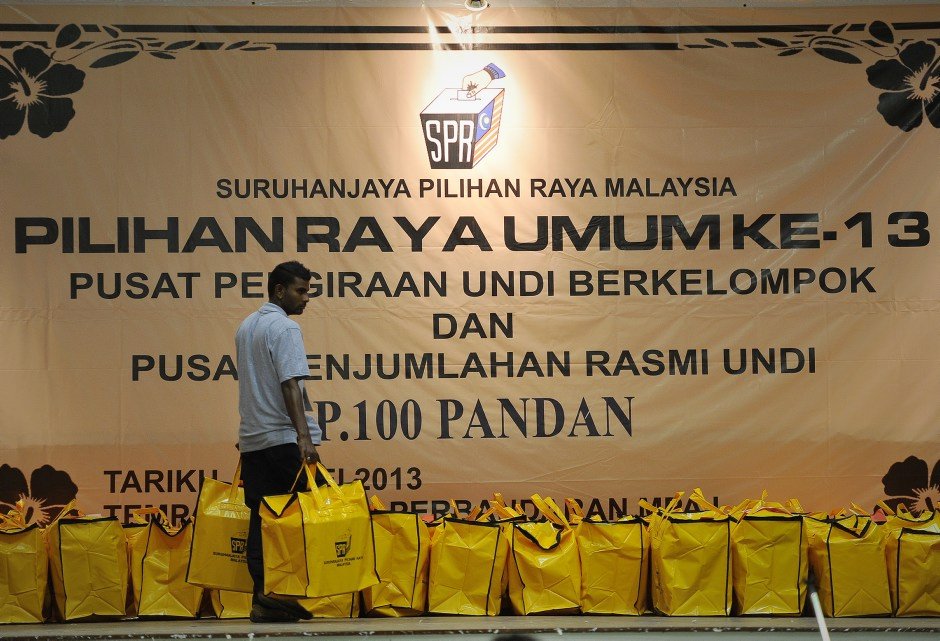 Yellow Election Commission bags lined up at a vote-tallying centre under an SPR banner, 2013
